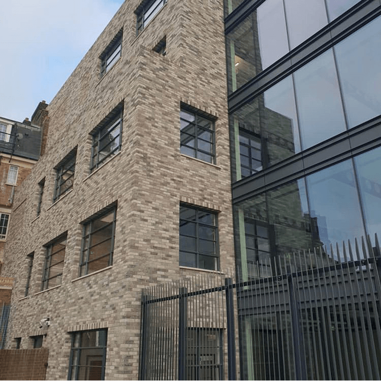 Modern building with a MCPV021 facade next to a traditional stone building, separated by a metal fence.
