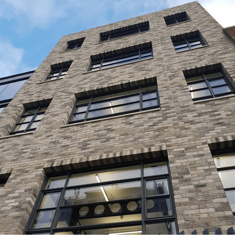 Modern multi-story building with large windows and a MCPV021 stone facade under a clear sky.