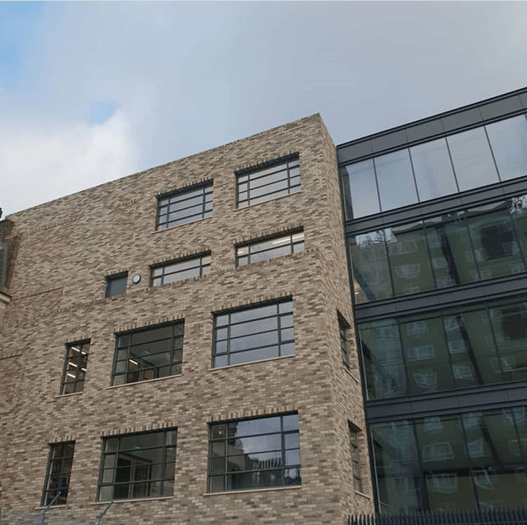 Modern brick building featuring large windows and a contrasting glass extension under a cloudy sky. (MCPV021)