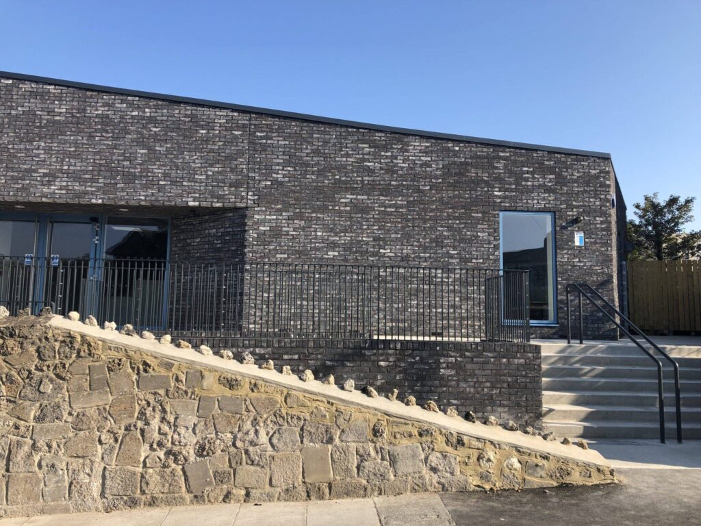 Modern building with MCPV069 walls, large windows, and a metal railing along stone steps under a clear sky.
