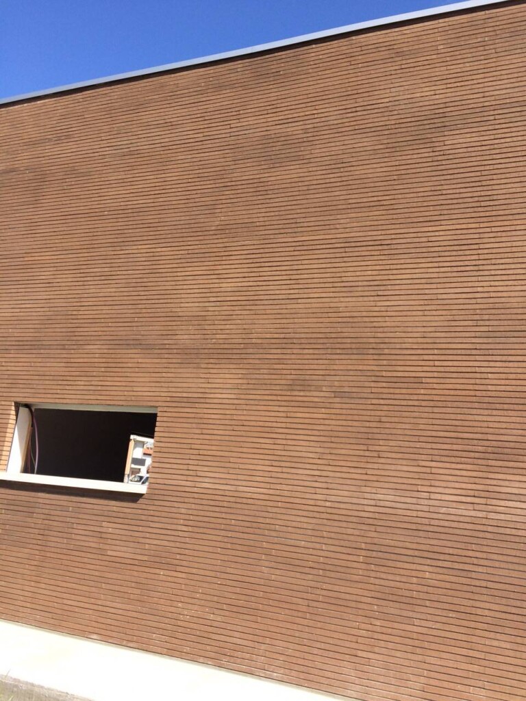 Exterior wall of a modern building with horizontal brown MCPV308 cladding and one asymmetrical window under a clear blue sky.