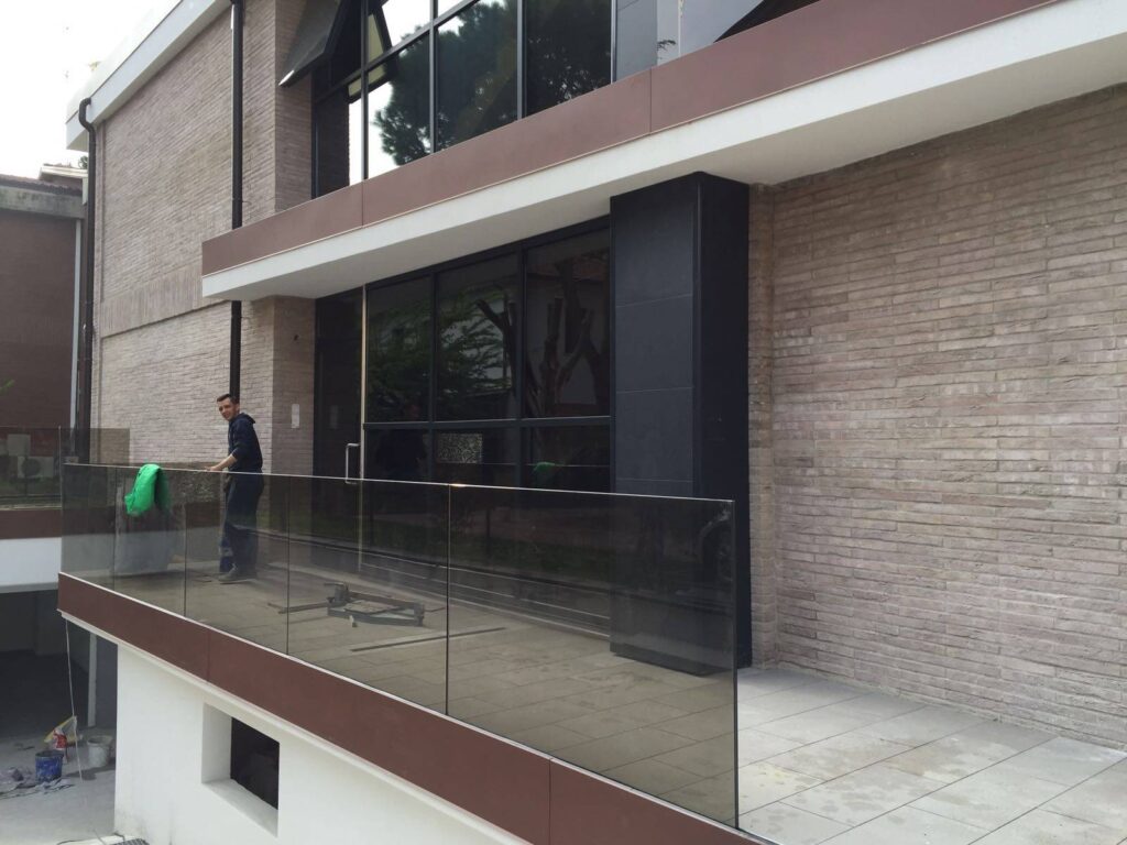 A modern building with large glass windows and a beige brick exterior, featuring an MCPV328 walking past and another cleaning the windows.