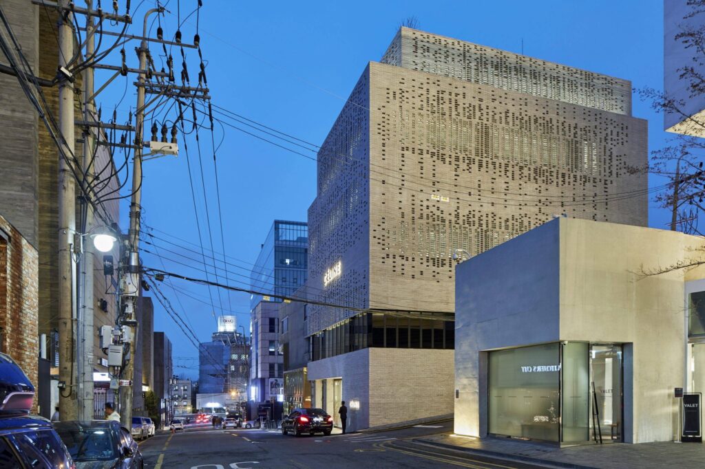 Exterior view of a modern building with a unique perforated facade, illuminated at dusk