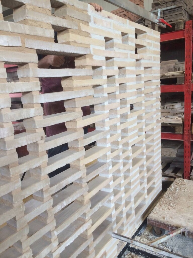 A worker partially visible through a large, intricate lattice of white bricks stacked in a warehouse