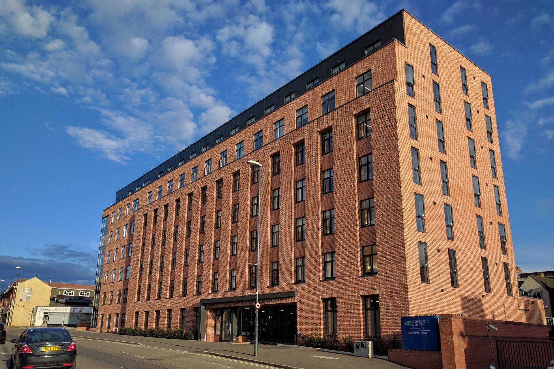 A six-story brick building with numerous windows, under a partly cloudy sky, next to a street