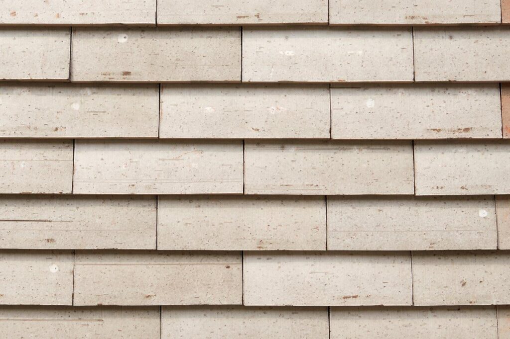 A textured wall made of overlapping beige stone tiles with visible screw heads.