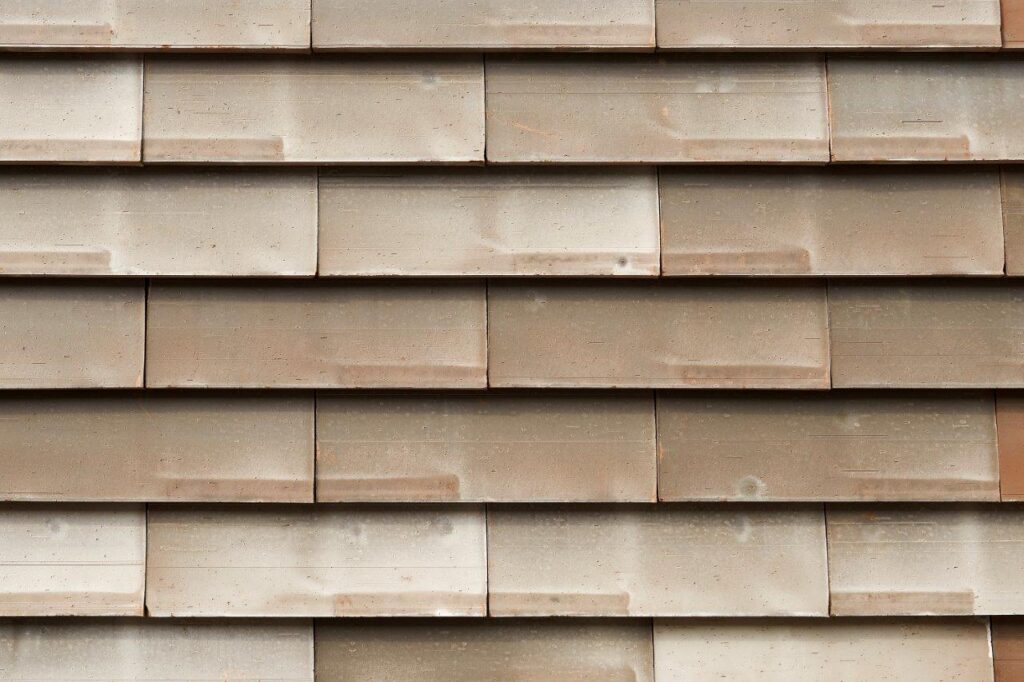 Close-up of a beige, textured tile wall with overlapping rectangular tiles arranged in a pattern.