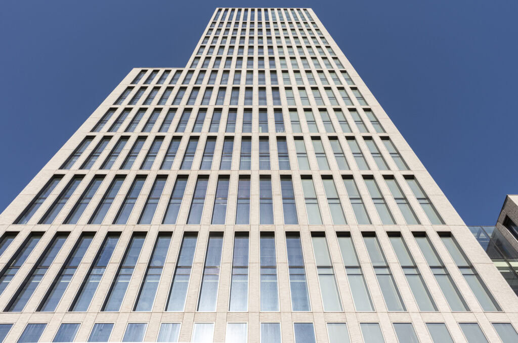 A low-angle view capturing the towering facade of a modern skyscraper against a clear blue sky.