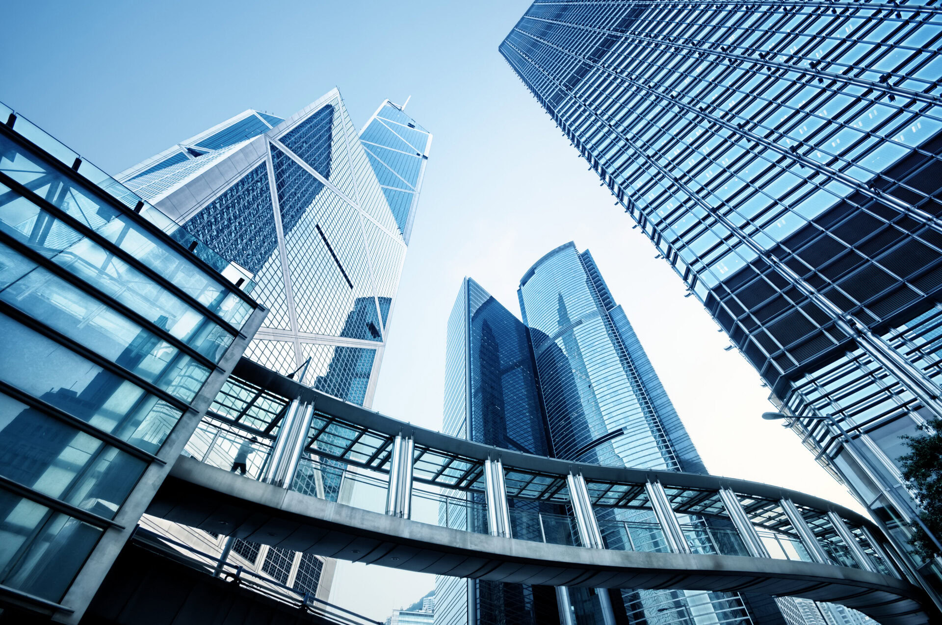 Low-angle view of modern skyscrapers with a connecting pedestrian bridge under a clear blue sky.
