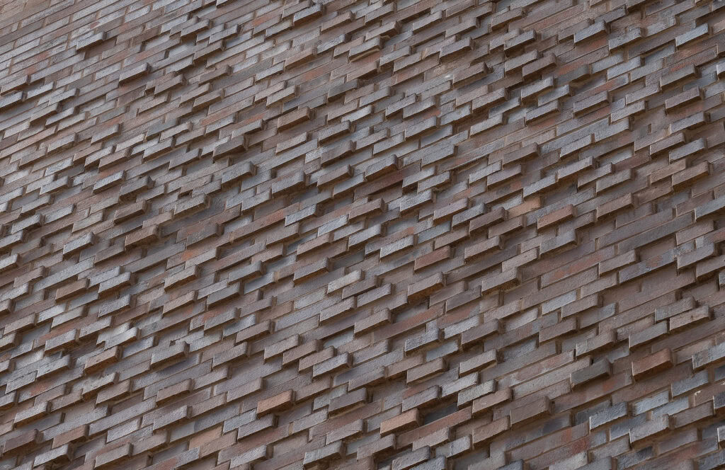 Close-up of a textured building facade made of overlapping rectangular tiles.