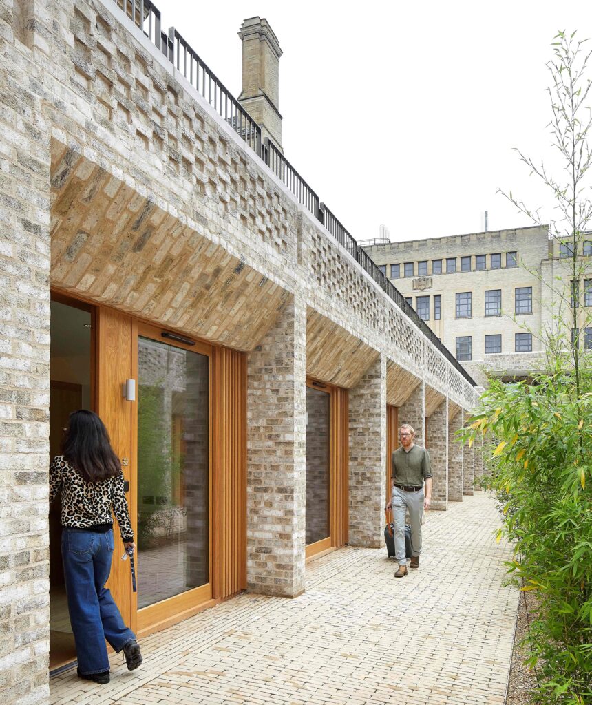 Two people walking near a modern building with large glass doors, surrounded by greenery of MCPV187.