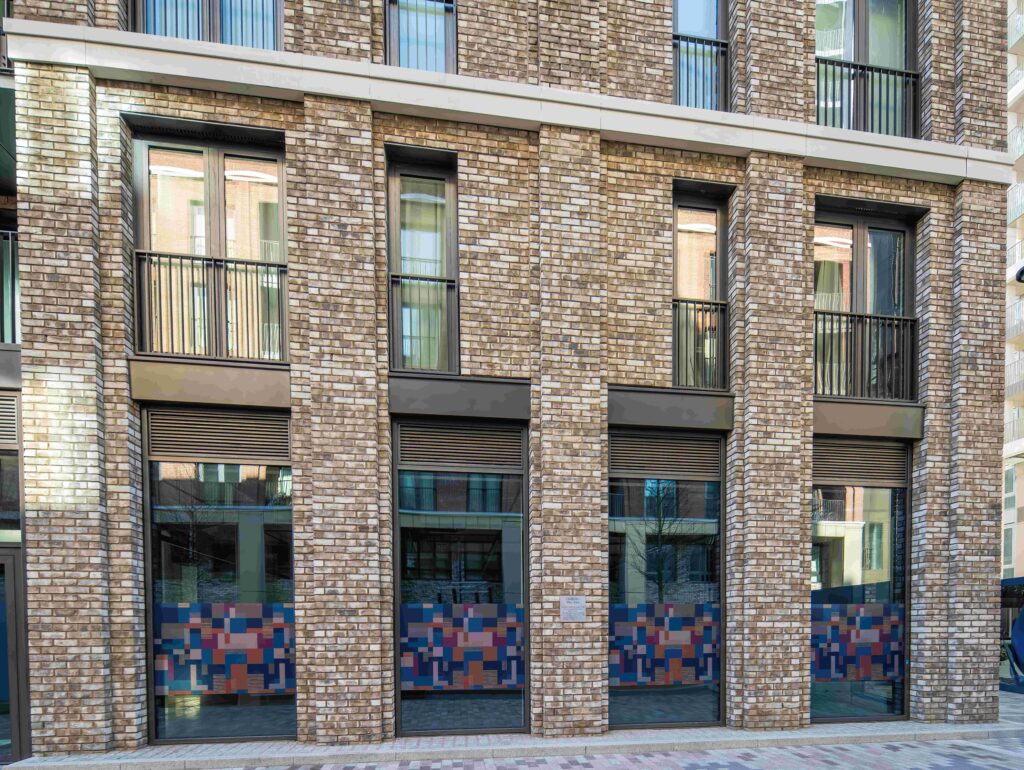Modern MCPV187 building facade with large glass windows and colorful mosaic tiles at the base.