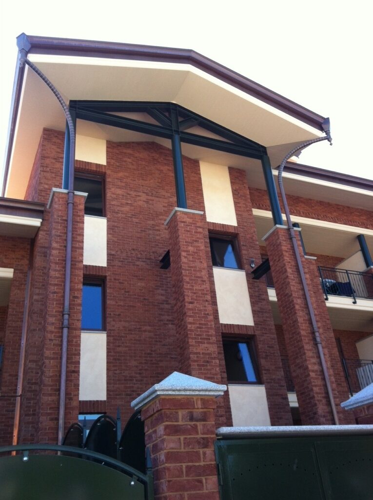 Three-story brick building with contrasting white columns, black-framed windows, and a curved metal roof MCPV133.