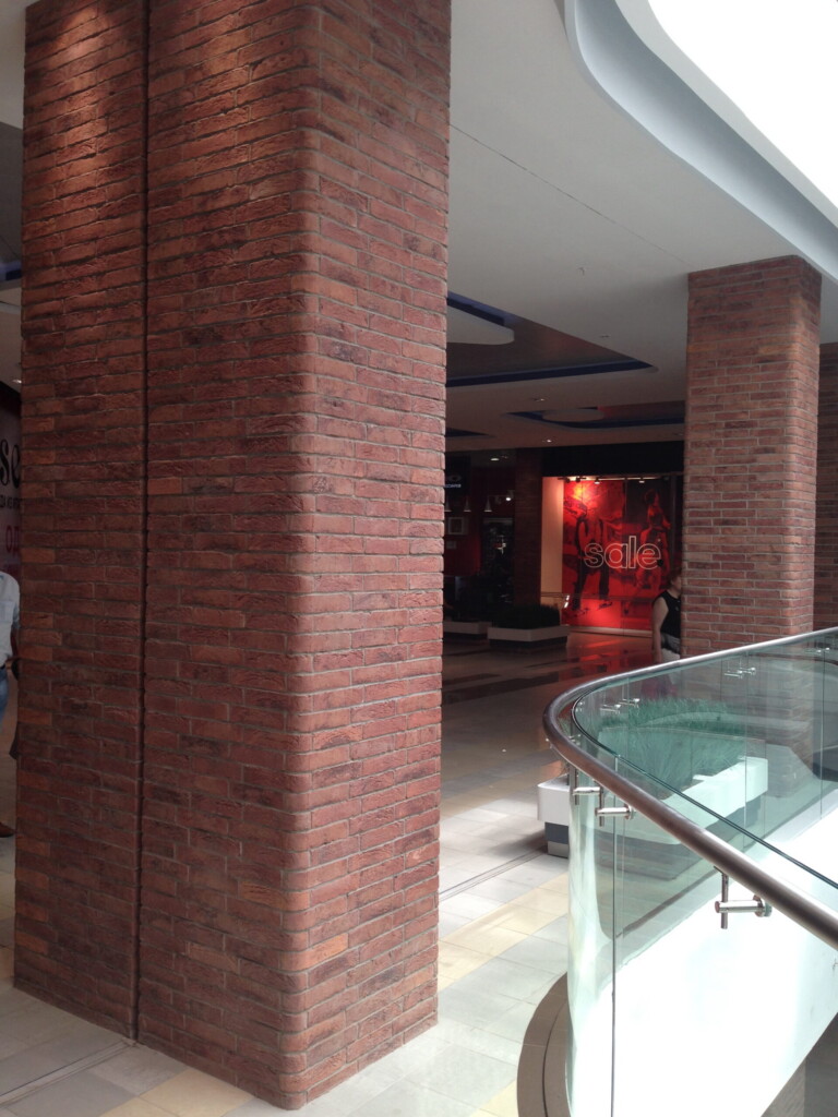 Interior of a shopping mall with brick columns and a glass railing on the right, visible MCPV133 sign in the background.