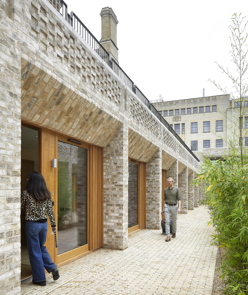 Two people walk along a walkway paved with bricks beside a modern building
