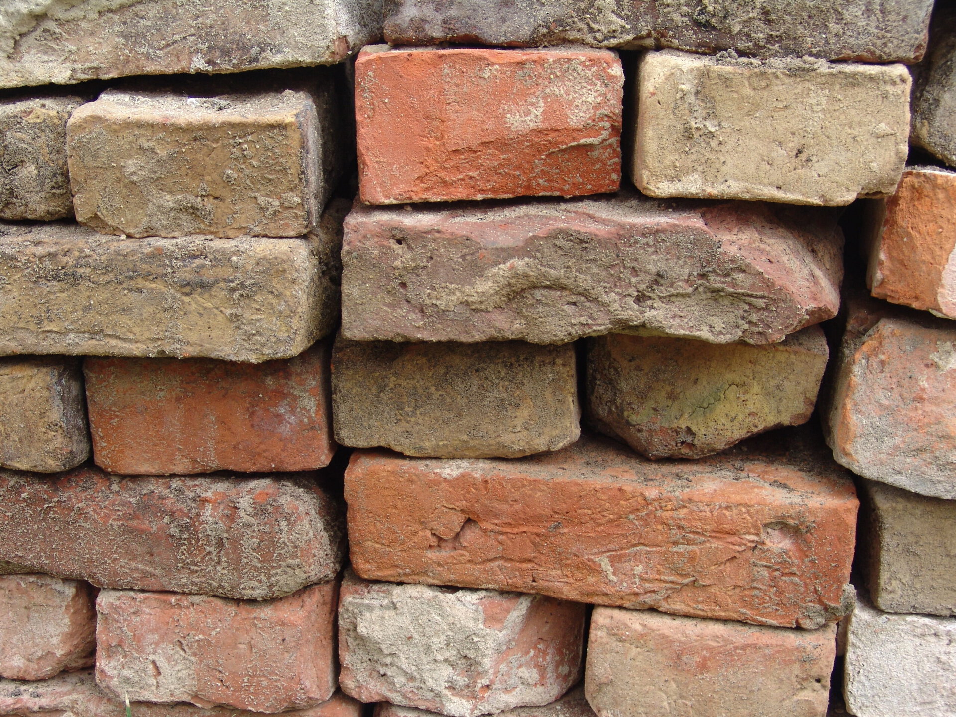 A stack of reclaimed clay bricks in mixed reds and buffs, salvaged from demolition for reuse
