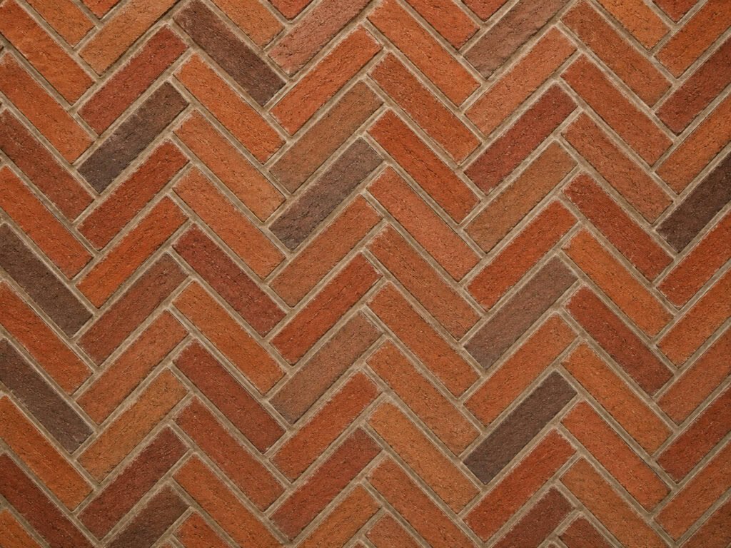 Herringbone brick pattern using mixed red, orange and brown clay bricks with pale mortar joints