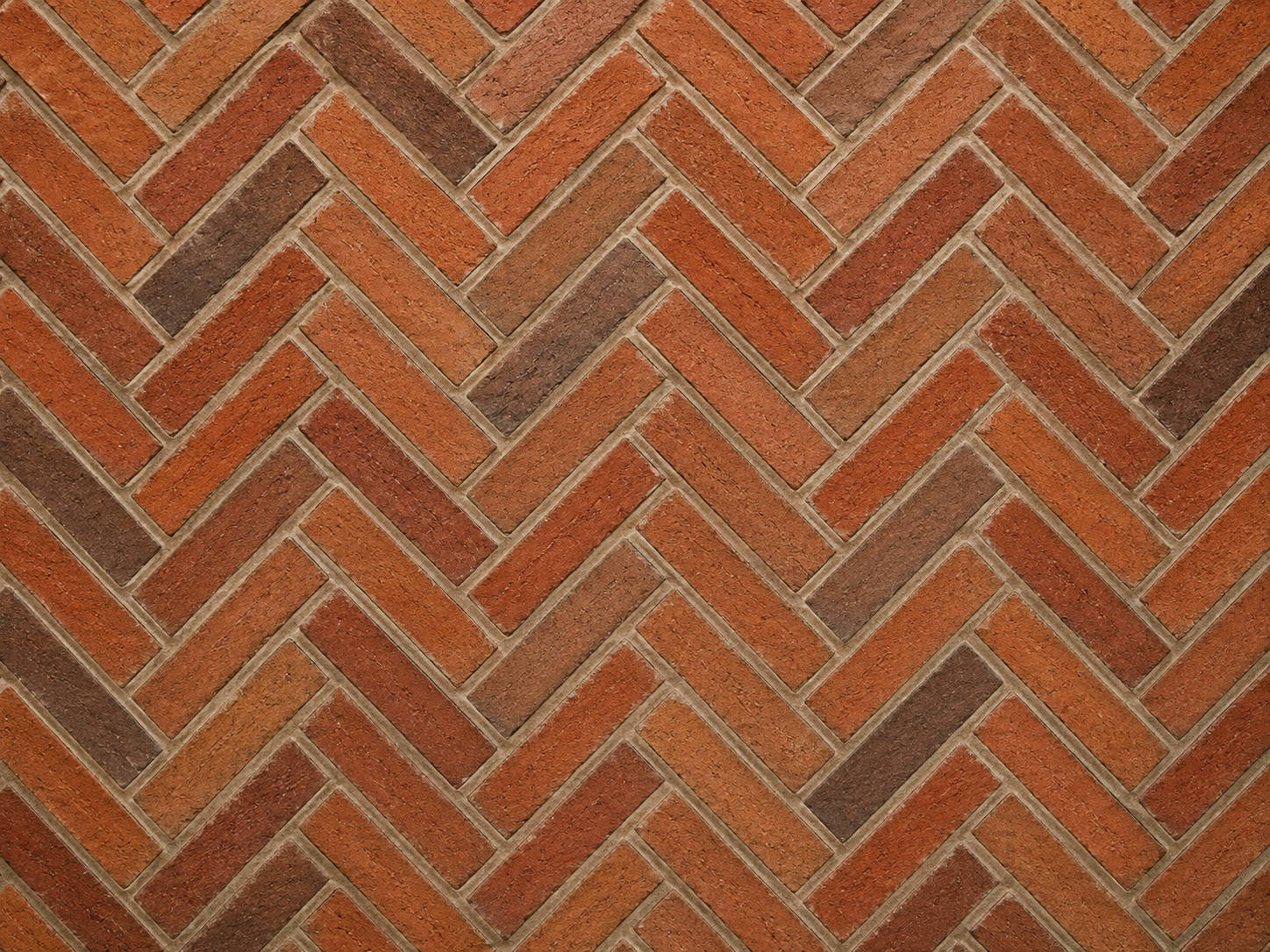 Herringbone brick pattern using mixed red, orange and brown clay bricks with pale mortar joints