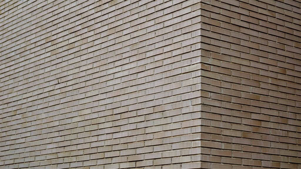 Long format brick façade in pale buff clay, the slim linear units wrapping a building corner