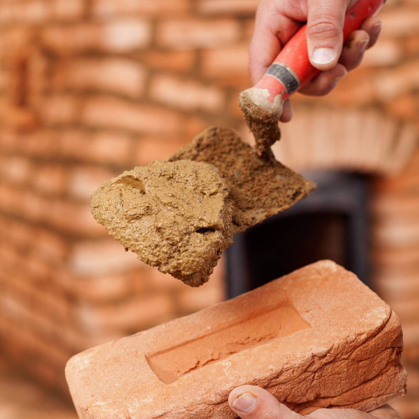 Masonry heater builder hand with brick, trowel and clay mortar